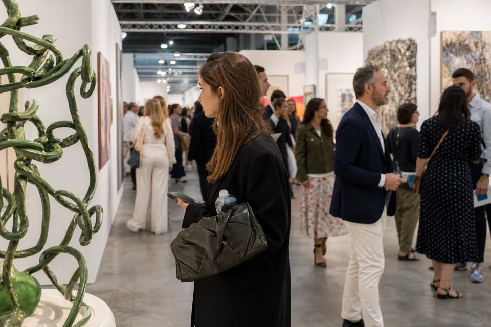 The aisle of a large art fair on preview day, with booths on both sides and collectors walking between them